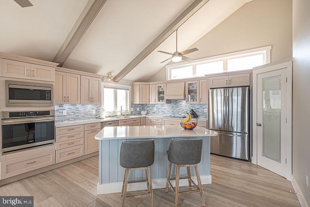 kitchen featuring stainless steel appliances, light countertops, glass insert cabinets, a sink, and light wood-type flooring