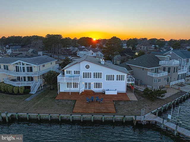 back of house at dusk with a yard, a patio, a water view, and a residential view