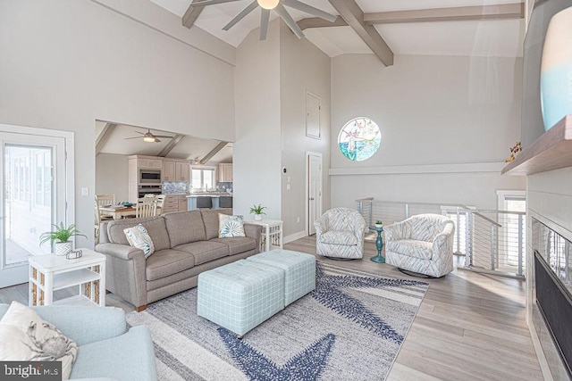 living area featuring high vaulted ceiling, light wood-type flooring, beamed ceiling, and ceiling fan