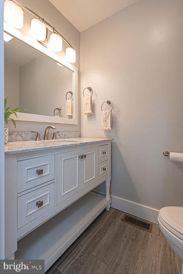 bathroom featuring baseboards, visible vents, wood finished floors, and vanity