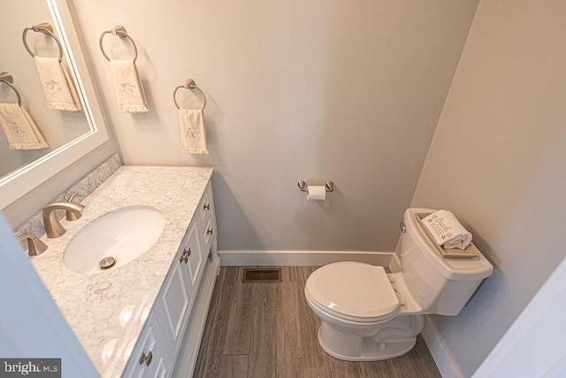 bathroom with baseboards, visible vents, toilet, wood finished floors, and vanity