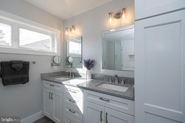 bathroom with double vanity, baseboards, a shower, and a sink