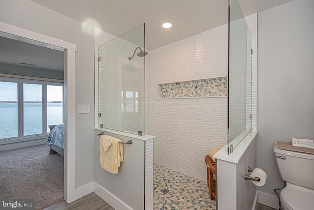 bathroom featuring a water view, toilet, ensuite bathroom, baseboards, and walk in shower