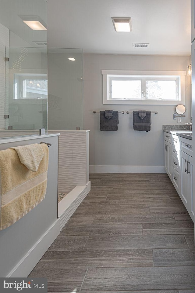 full bath with wood finished floors, walk in shower, visible vents, and baseboards