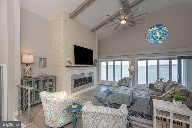 living area featuring high vaulted ceiling, a glass covered fireplace, beamed ceiling, and wood finished floors