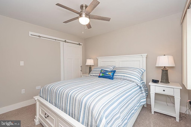 bedroom with a barn door, a ceiling fan, light colored carpet, and baseboards