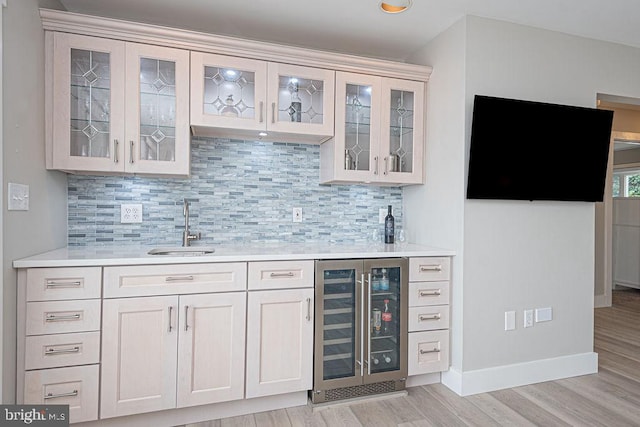 bar with beverage cooler, a sink, light wood finished floors, tasteful backsplash, and indoor wet bar