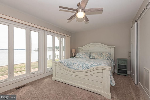 carpeted bedroom featuring a water view, access to outside, visible vents, and a ceiling fan