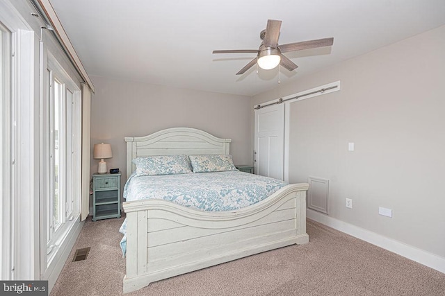 bedroom with a barn door, visible vents, baseboards, ceiling fan, and carpet floors