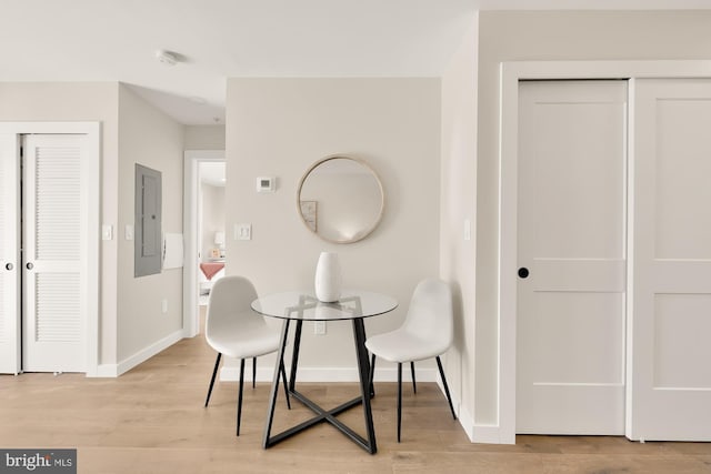 dining space with baseboards, electric panel, and light wood-style floors