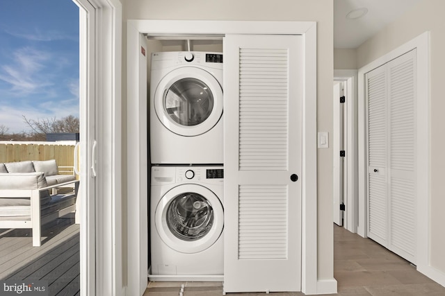 clothes washing area featuring laundry area, wood finished floors, and stacked washer and clothes dryer