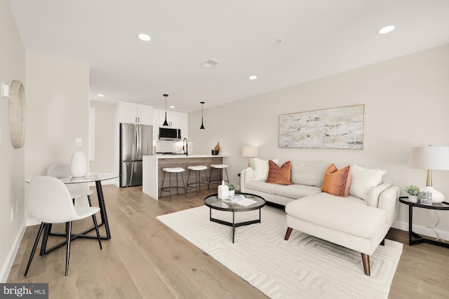 living area with light wood-type flooring, visible vents, baseboards, and recessed lighting