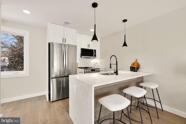 kitchen featuring light wood-style flooring, a peninsula, a sink, appliances with stainless steel finishes, and a kitchen bar