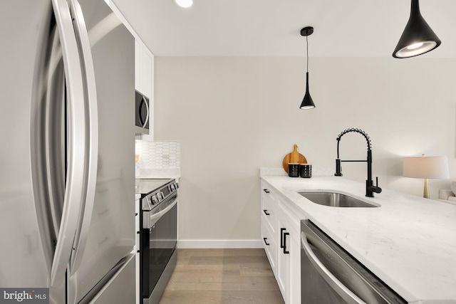 kitchen featuring backsplash, appliances with stainless steel finishes, white cabinetry, a sink, and wood finished floors