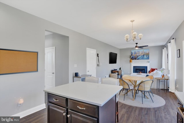 kitchen featuring light countertops, dark wood-type flooring, dark brown cabinetry, a glass covered fireplace, and ceiling fan with notable chandelier