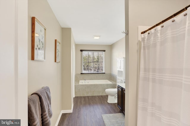 bathroom featuring tiled bath, toilet, wood finished floors, and vanity