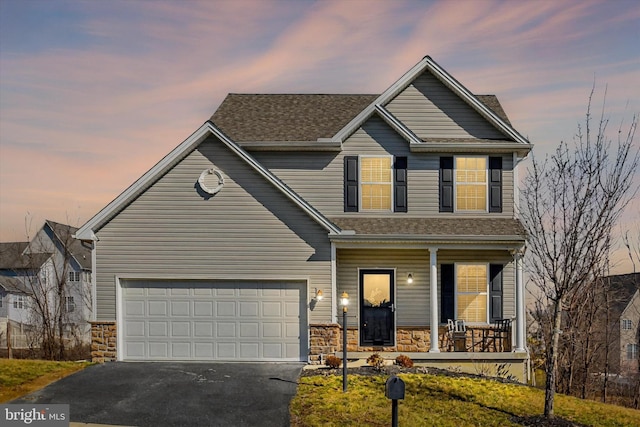 traditional-style house with a shingled roof, a porch, a garage, stone siding, and driveway