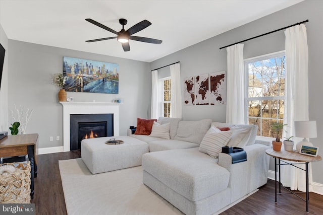 living area with a glass covered fireplace, dark wood-style floors, baseboards, and ceiling fan