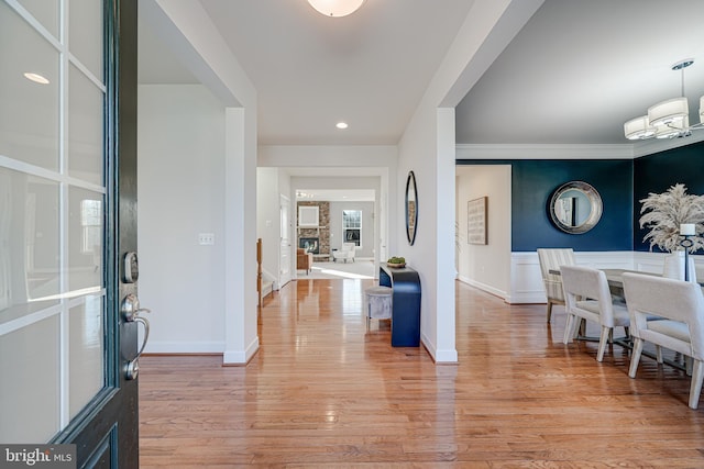 entrance foyer featuring a notable chandelier, a stone fireplace, light wood finished floors, and baseboards