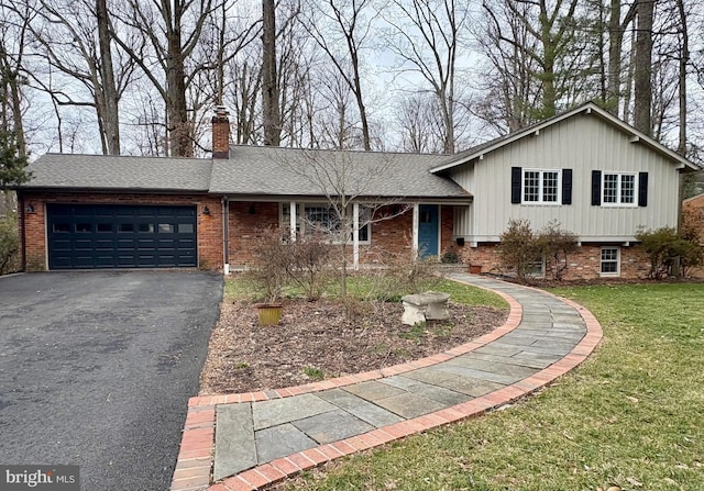 tri-level home with brick siding, a front lawn, a chimney, a garage, and driveway