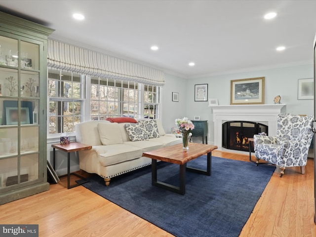 living area with crown molding, recessed lighting, wood finished floors, and a warm lit fireplace