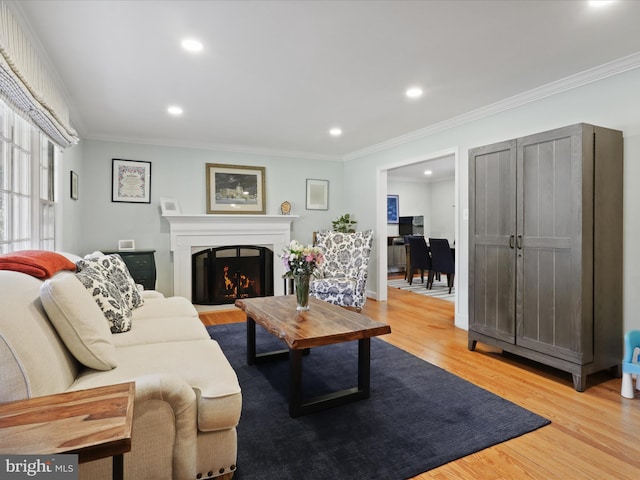 living area with recessed lighting, a warm lit fireplace, ornamental molding, and light wood finished floors