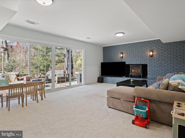 carpeted living room featuring visible vents, wainscoting, and a wood stove