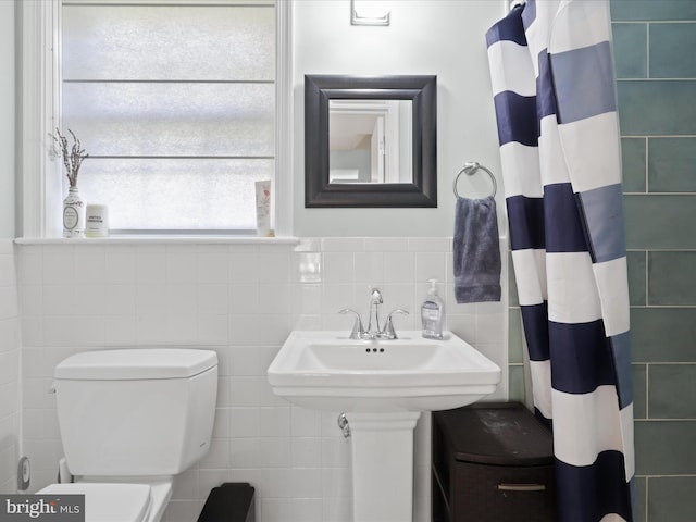 bathroom featuring wainscoting, toilet, curtained shower, and tile walls