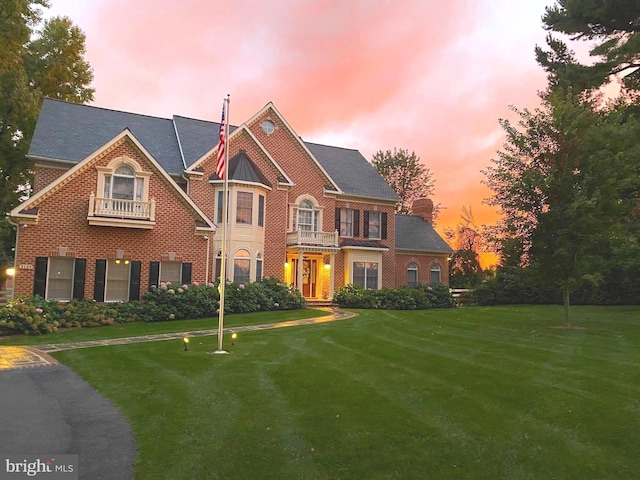 colonial home featuring brick siding, a front yard, and a balcony