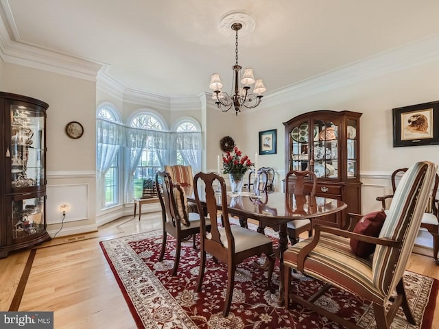 dining area with a chandelier, light wood-type flooring, wainscoting, and crown molding