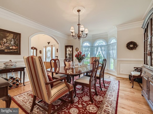 dining room with an inviting chandelier, arched walkways, a wainscoted wall, and ornamental molding