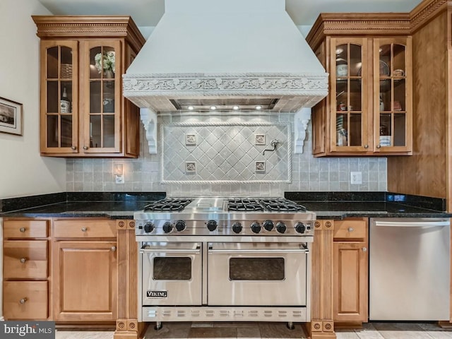 kitchen with stainless steel appliances, custom range hood, decorative backsplash, glass insert cabinets, and dark stone countertops