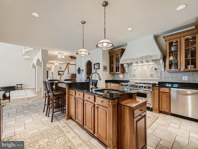 kitchen with arched walkways, stainless steel appliances, backsplash, a sink, and premium range hood