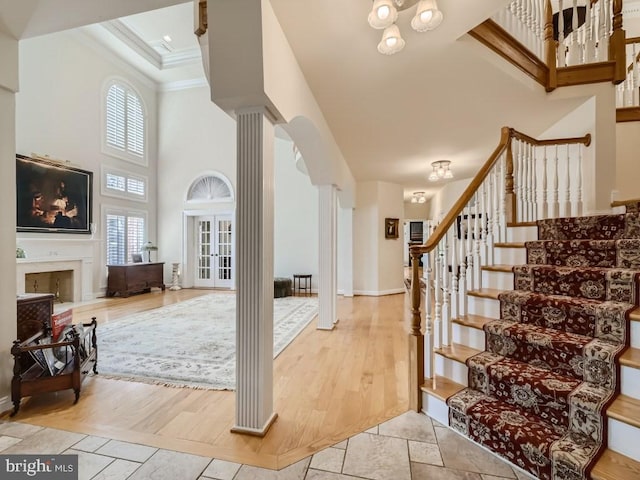 entryway with a fireplace, crown molding, stairway, a towering ceiling, and ornate columns