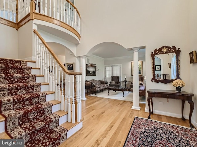 foyer entrance featuring crown molding, wood finished floors, a towering ceiling, and ornate columns