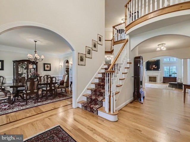 entrance foyer featuring crown molding, a fireplace, a towering ceiling, an inviting chandelier, and wood finished floors