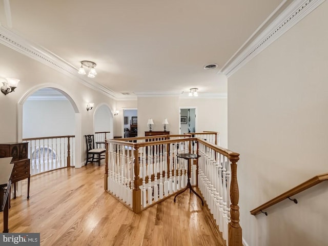 hall featuring light wood-type flooring, visible vents, ornamental molding, and an upstairs landing