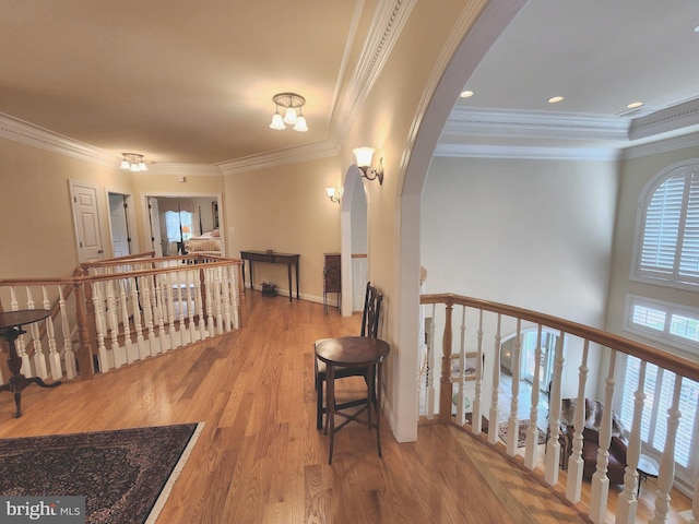 hall with ornamental molding, arched walkways, wood finished floors, and an upstairs landing