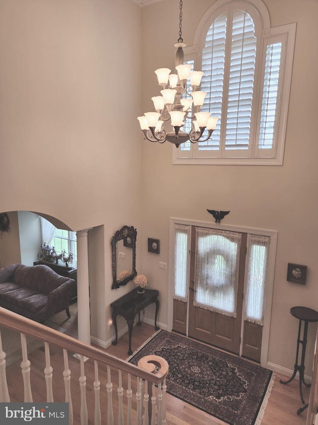 entrance foyer featuring baseboards, arched walkways, wood finished floors, a high ceiling, and a notable chandelier