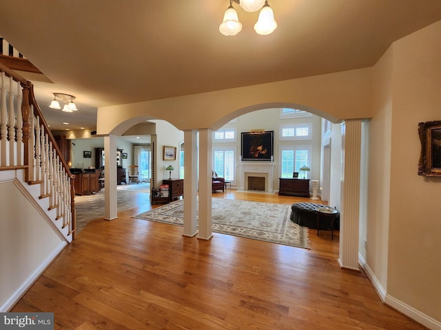 foyer entrance with a fireplace, wood finished floors, baseboards, stairs, and an inviting chandelier