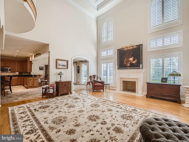 living room featuring a fireplace with flush hearth, arched walkways, light wood-style flooring, and crown molding