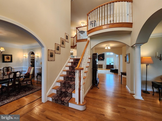 staircase featuring arched walkways, wood finished floors, decorative columns, and crown molding