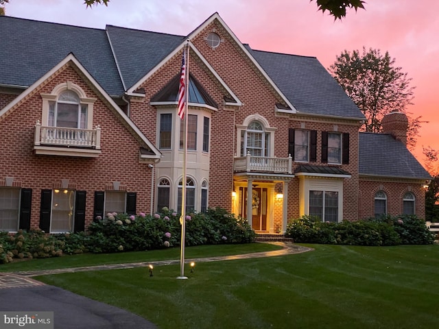 view of front facade with a chimney, brick siding, a yard, and a balcony