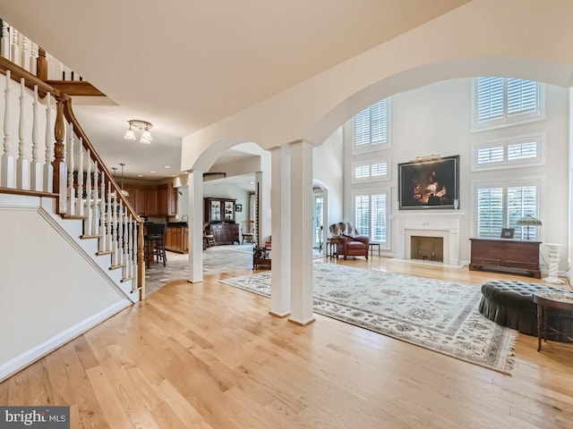 entrance foyer with a high ceiling, a fireplace, wood finished floors, stairway, and ornate columns