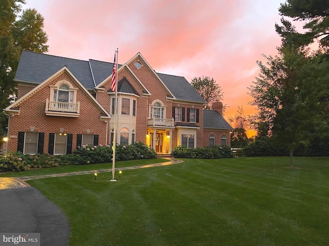 colonial house with brick siding, a lawn, and a balcony