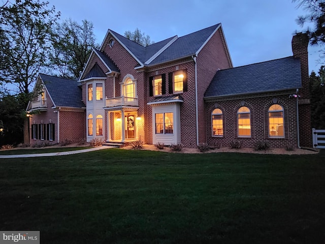 view of front of home featuring brick siding, a chimney, a front yard, and a balcony