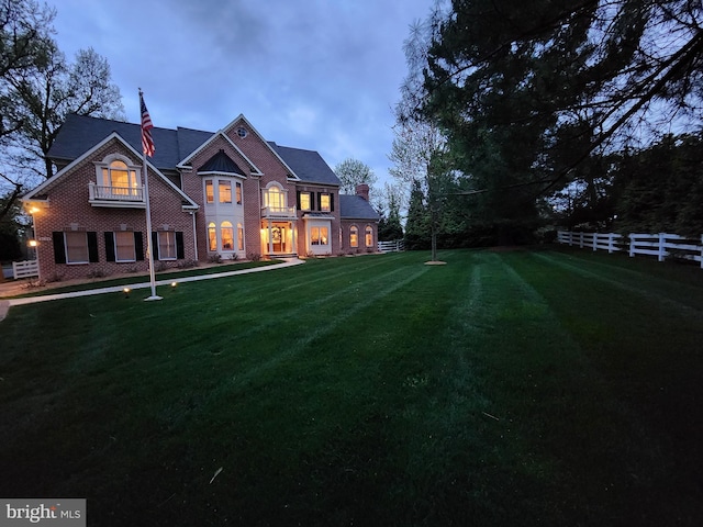 rear view of house featuring brick siding, a chimney, fence, and a yard