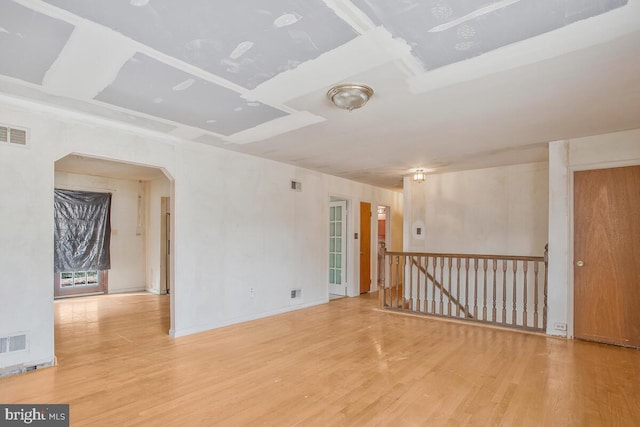 empty room with arched walkways, wood finished floors, and visible vents