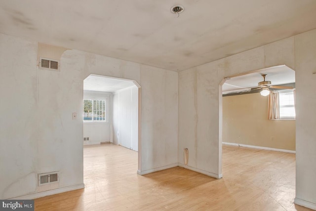 unfurnished room featuring arched walkways, visible vents, ceiling fan, and light wood-style flooring