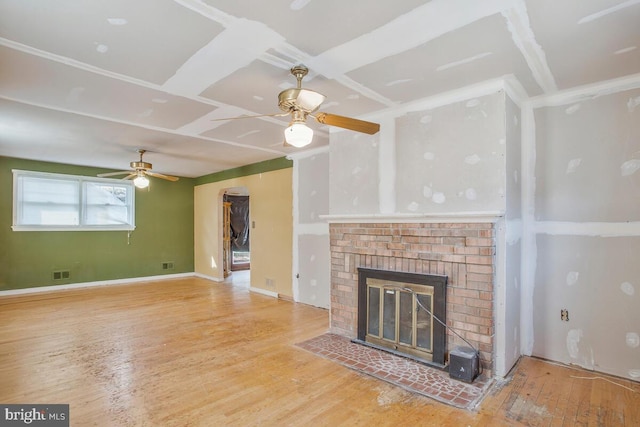 unfurnished living room with a brick fireplace, baseboards, visible vents, and wood finished floors